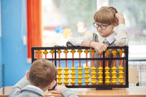 young schoolgirl with glasses helps a friend use abacus soroban