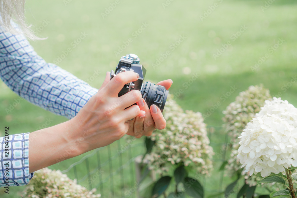 The blonde girl is holding an antique camera and focuses on a white flower