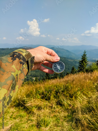 Man in military clothes holding a compass in a hand on the carpathian mountains background