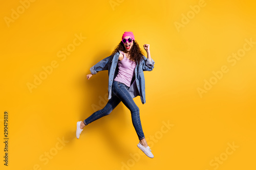 Fototapeta Naklejka Na Ścianę i Meble -  Full body photo of stylish wavy lady jumping high running quickly to shopping center wear casual trendy clothes isolated yellow color background
