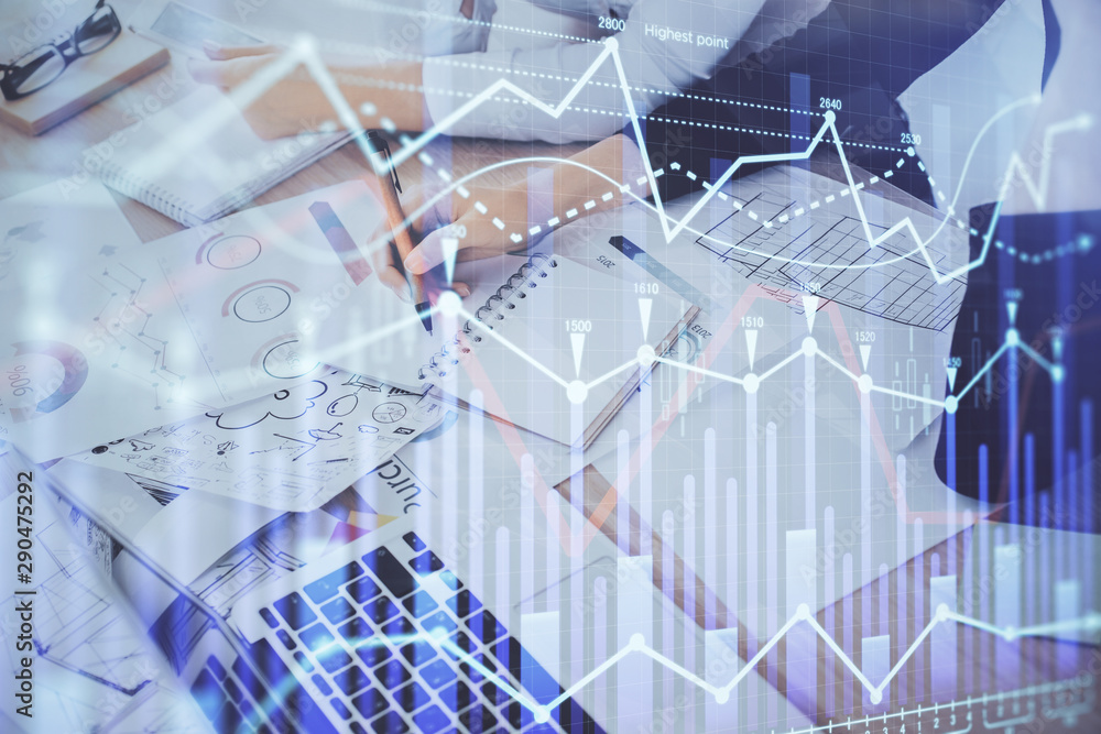 A woman hands writing information about stock market in notepad. Forex chart holograms in front. Concept of research. Double exposure A woman hands writing information about stock market in notepad. Forex chart holograms in front. Concept of research. Double exposure