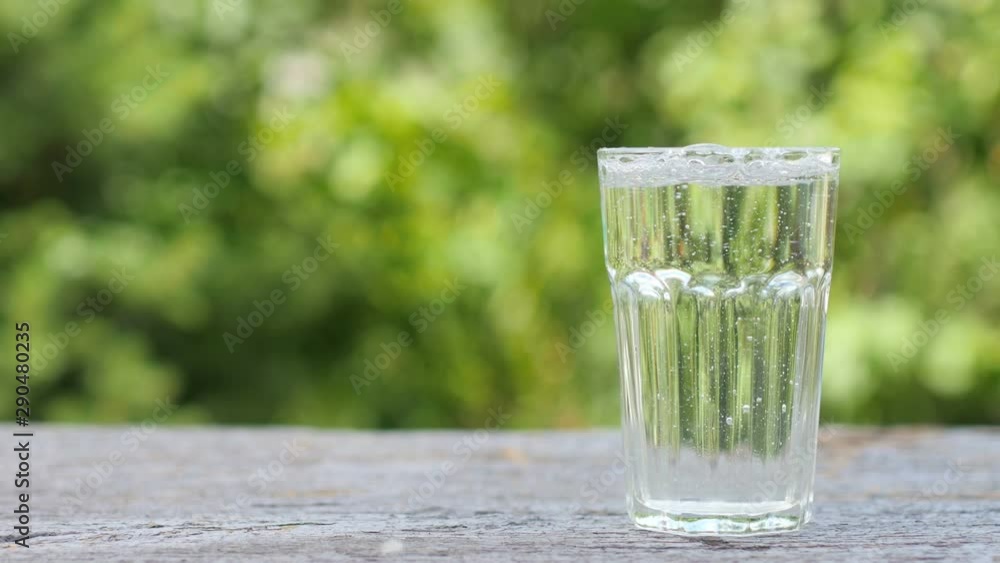 Fresh clean water is poured into a glass standing on a wooden table, on a natural green background. health and diet concept Fresh clean water is poured into a glass standing on a wooden table, on a natural green background. health and diet concept