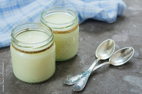 Greek yogurt in glass jars with spoons on a gray textural background.