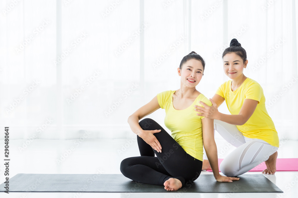 Two young Asian women workout practicing yoga in yellow dress or pose with a trainer and practice meditation wellness lifestyle and health fitness concept in a gym. Two young Asian women workout practicing yoga in yellow dress or pose with a trainer and practice meditation wellness lifestyle and health fitness concept in a gym.
