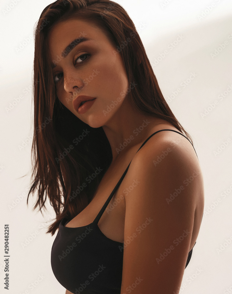 Foto de Closeup portrait of beautiful sexy girl in black summer bra.Tanned  slim woman posing in studio near white wall. Hot brunette model in swimwear  do Stock