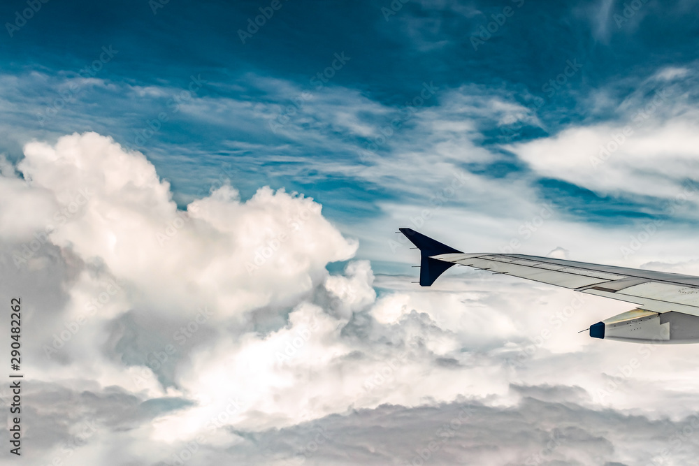 Fototapeta premium Mesmerizing natural view from Window side of an Airplane, cruising through White and Furry Cumulus Clouds with clear blue sky above it. Airplane wing parts flaps, pylon and winglet is visible - Image
