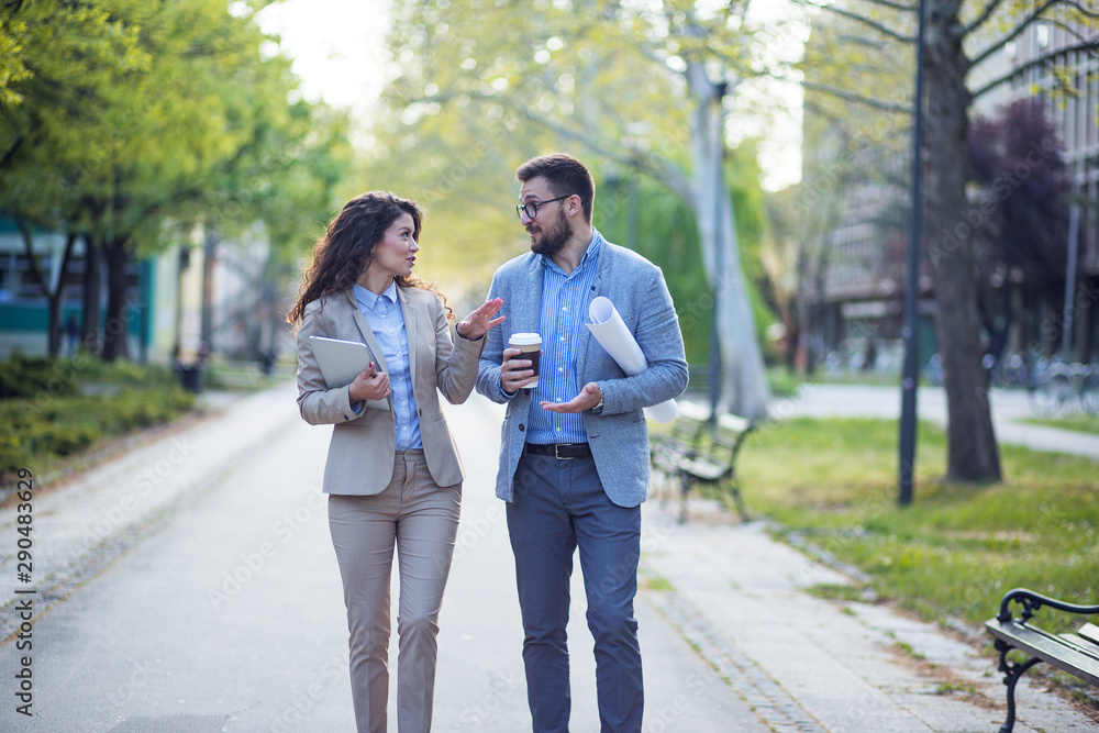 Fototapeta premium Businesswoman and businessman walking in a park and discussing