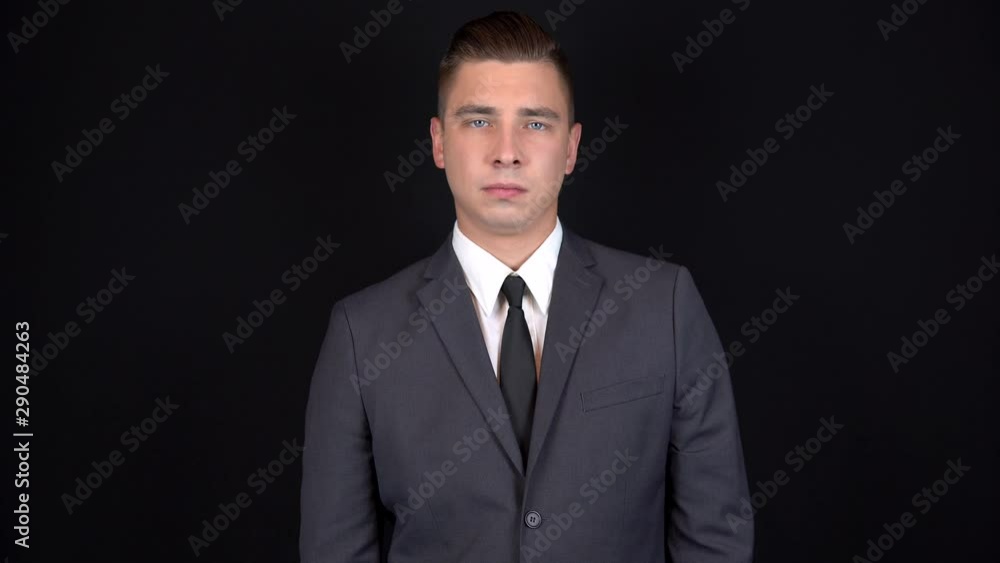 Young businessman shows a hand gesture approximately. Man in a black suit on a black background Young businessman shows a hand gesture approximately. Man in a black suit on a black background