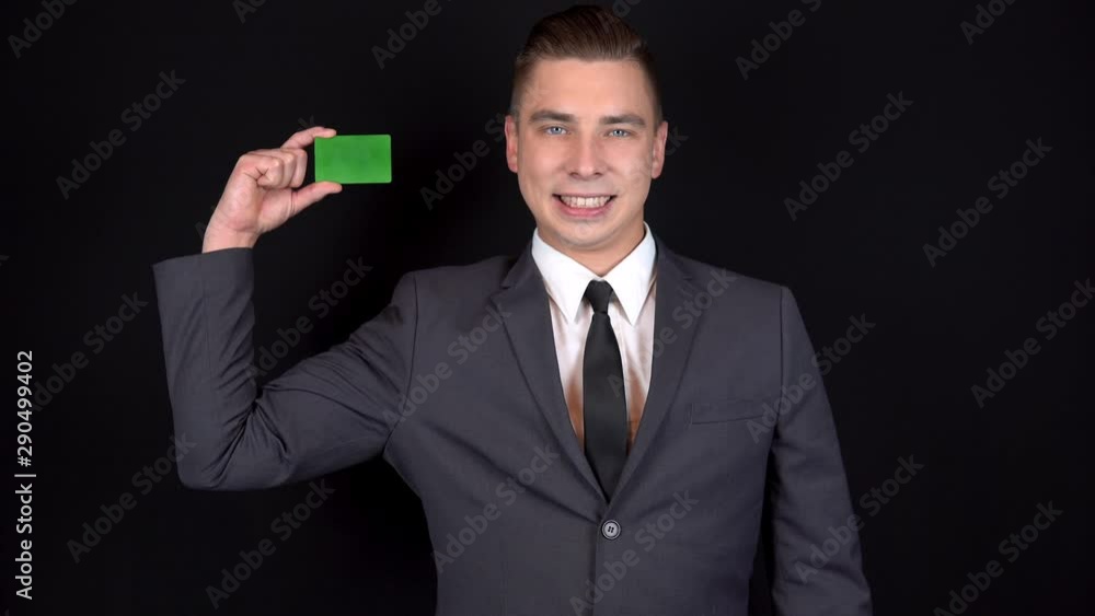 A young businessman presents a green bank card. Chromakey green card. Man in a black suit on a black background A young businessman presents a green bank card. Chromakey green card. Man in a black suit on a black background