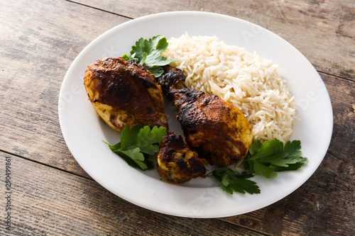 Roasted tandoori chicken with basmati rice in plate on wooden table.