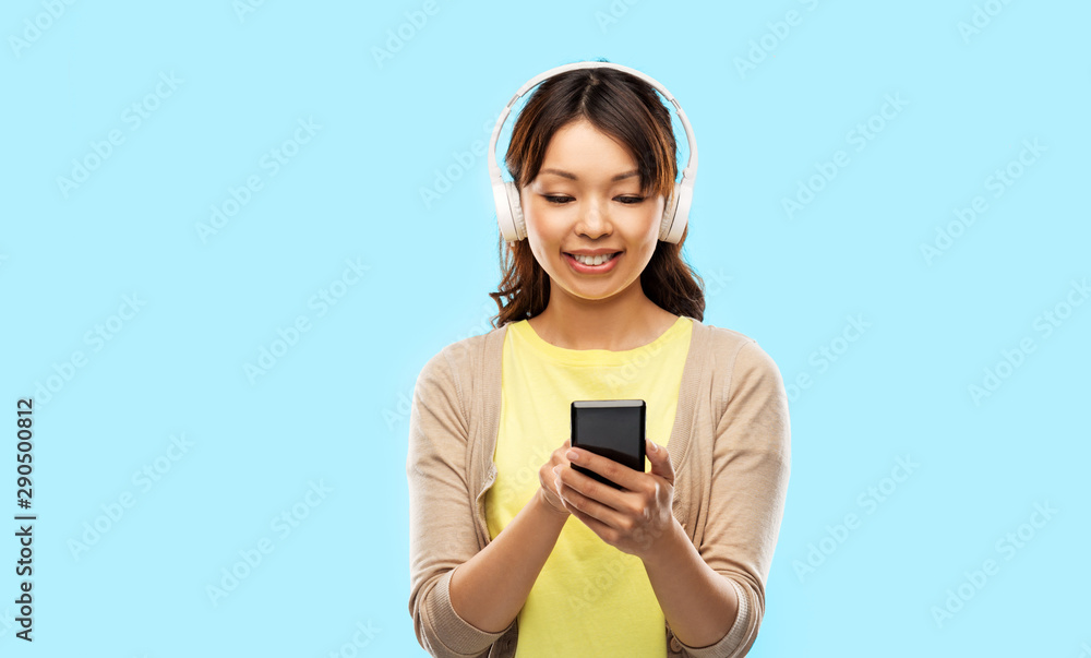 people, technology and audio equipment concept - happy asian young woman in headphones listening to music on smartphone over blue background people, technology and audio equipment concept - happy asian young woman in headphones listening to music on smartphone over blue background