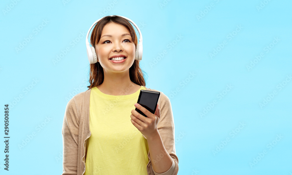 people, technology and audio equipment concept - happy asian young woman in headphones listening to music on smartphone over blue background people, technology and audio equipment concept - happy asian young woman in headphones listening to music on smartphone over blue background