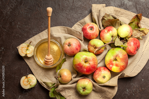 Ripe garden striped apples with leaves and a jar of honey on a beige napkin and textured background. Autumn harvest