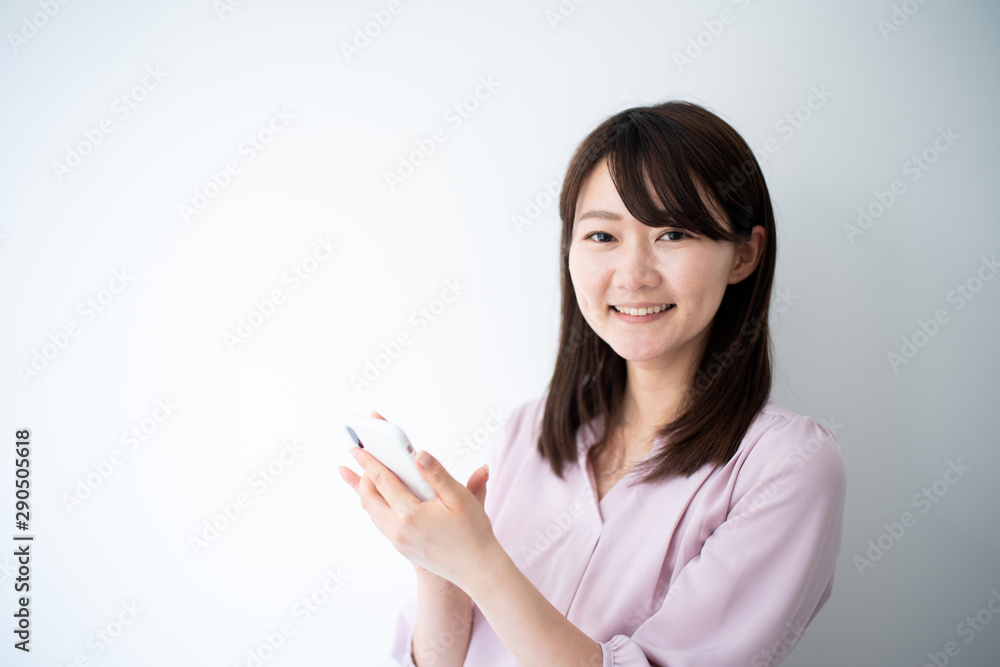 Young business woman holding smart phone against white wall Young business woman holding smart phone against white wall
