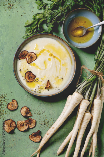 Canvas Print Parsnip cream soup in ceramic bowl with sun dried pears, butter sauce, bundle of fresh parsnip and herbs over green texture background