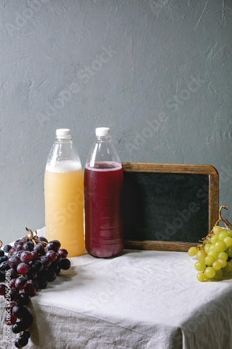 Traditional New european low alcohol red and white wine Federweisser, Neuer Wein, Burcak, Vin bourru in plastic bottles with black and green grapes on white table cloth. Empty chalkboard with space. photo