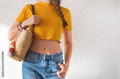 Young woman wearing yellow t-shirt and holding straw handbag against white wall Fototapet