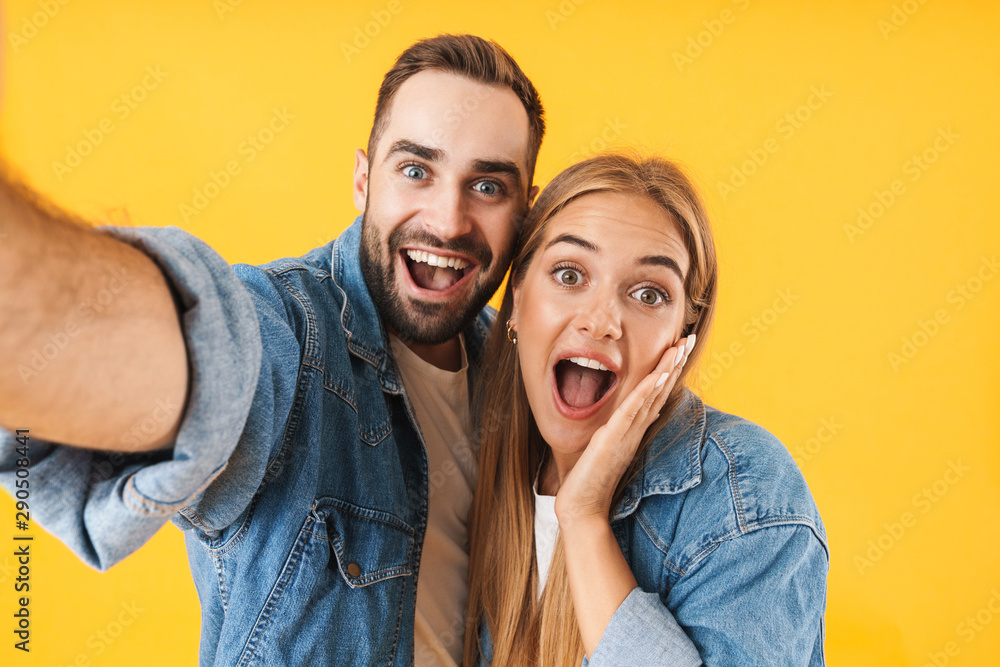 Image of optimistic couple smiling at camera while taking selfie photo Image of optimistic couple smiling at camera while taking selfie photo