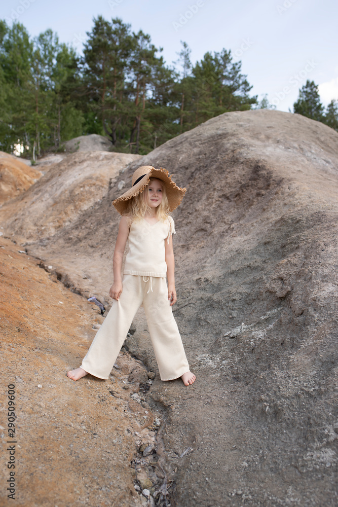 Naklejka premium Little cute girl in stylish clothes on a background of rocks. Summer portrait of a little girl in a hat and cotton clothes for a magazine or advertisement