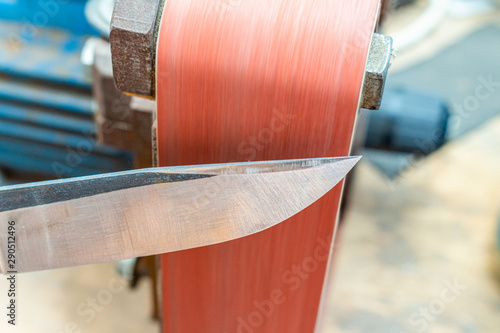 Fototapet Grinding polishing sharpening knife blade on the belt grinder sander equipment