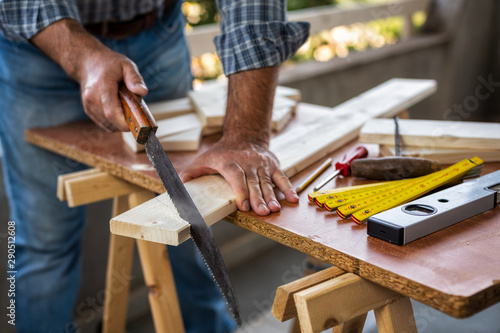 Adult craftsman carpenter with manual saw working on cutting a wooden table. Housework do it yourself. Stock photography.