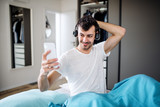 Young man with headphones and smartphone in bed at home, listening to music.