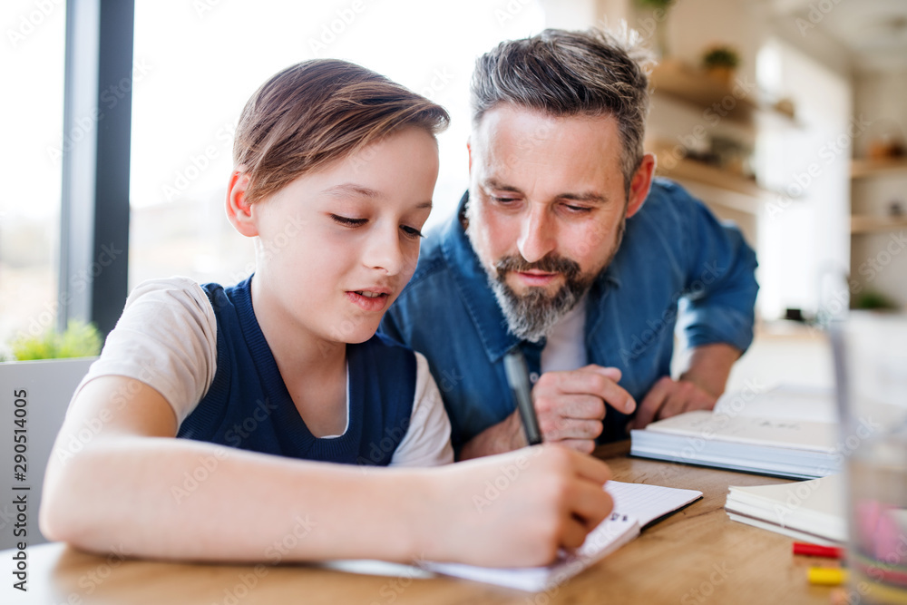 Mature father with small son sitting at table indoors, doing homework. Mature father with small son sitting at table indoors, doing homework.
