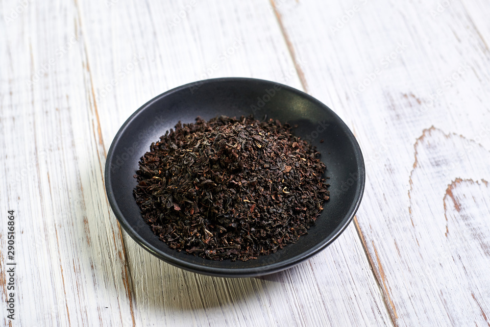 Black dry tea in a clay bowl on a light wooden background. Black dry tea in a clay bowl on a light wooden background.