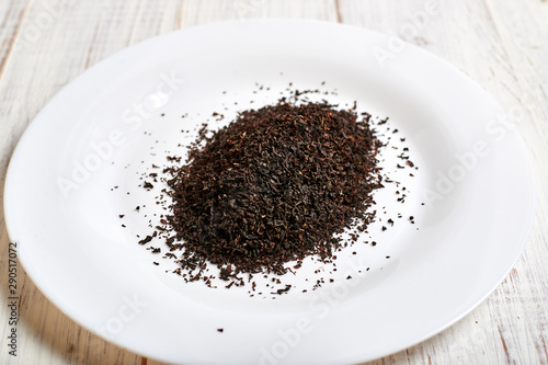 black dry tea on a white plate on a light wooden background.