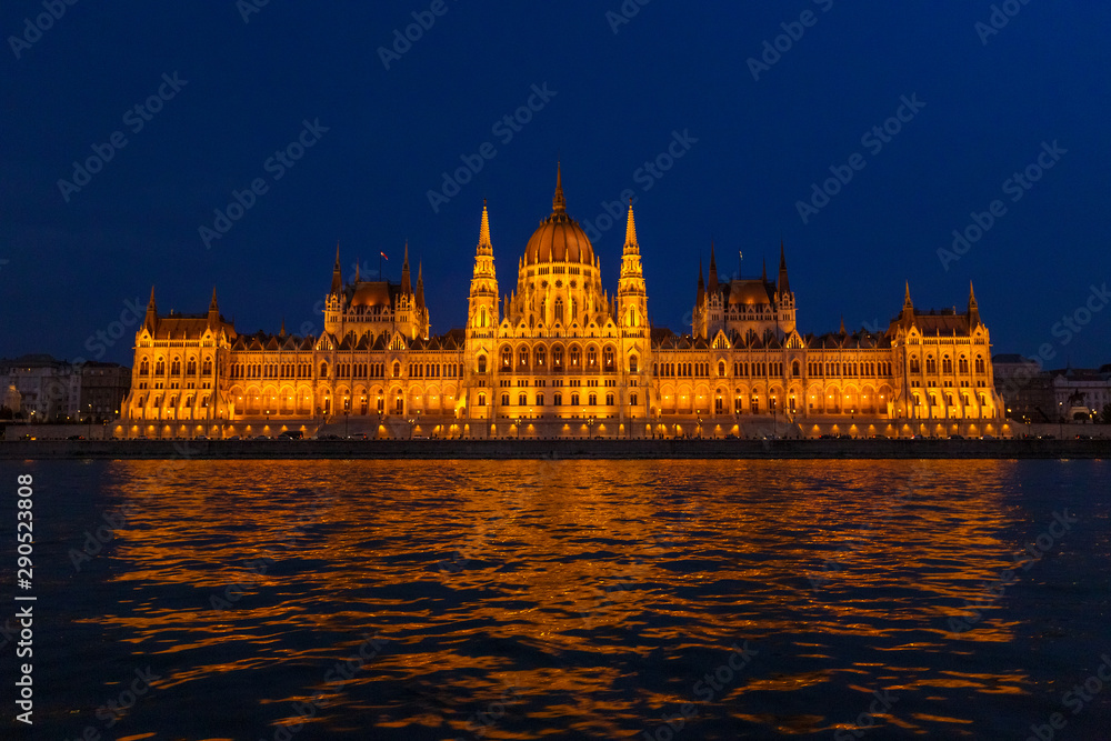 The Hungarian Parliament Building, a notable landmark of Hungary in Budapest. View of the main facade illuminated above the Danube river at night.