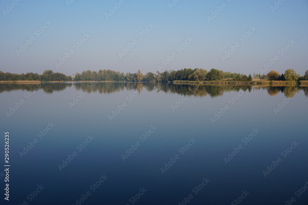 Autumnally discolored trees reflecting in the calm waters of the lake on an autumn afternoon in a small Polish town Lipiany in the West Pomeranian