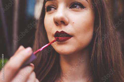 Beautiful young girl paints lips with lipstick