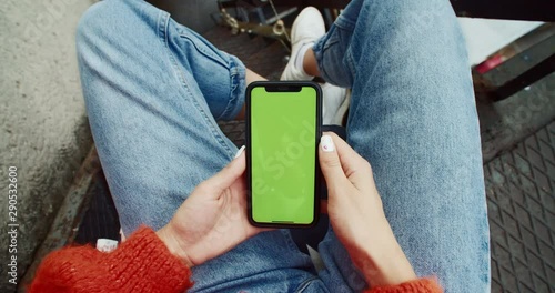 Close-up trendy girl chatting in social network on modern smartphone gadget mock-up chromekey green touchscreen outdoor. photo