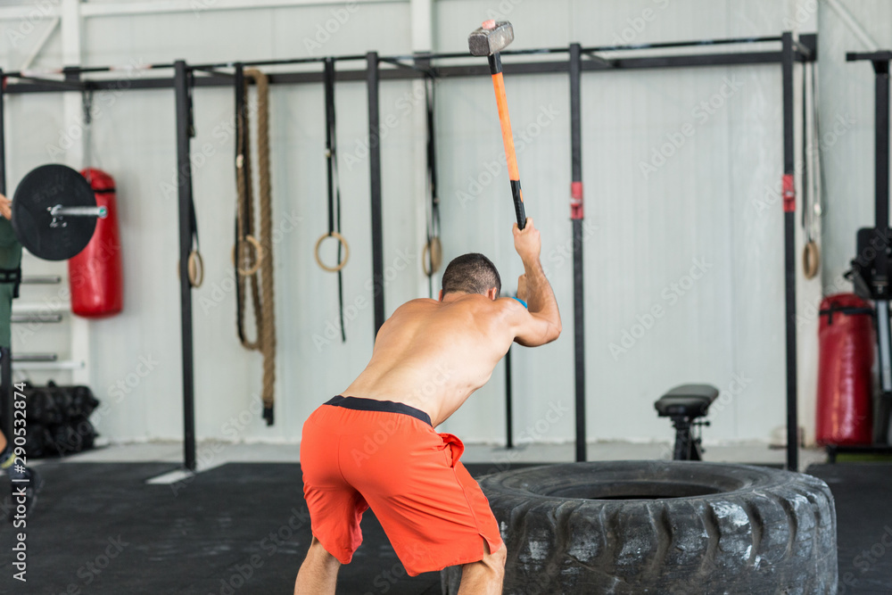 Fototapeta premium Sport fitness man hitting tractor tire with a sledgehammer