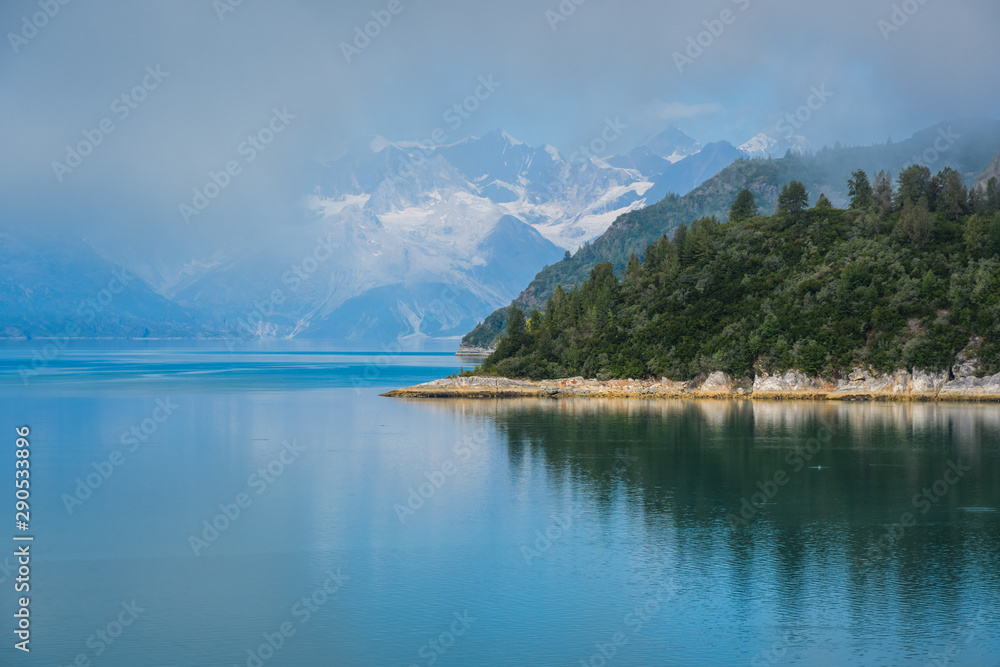 Remote coastline in misty Alaskan inside passage fjord with snow capped mountains in background