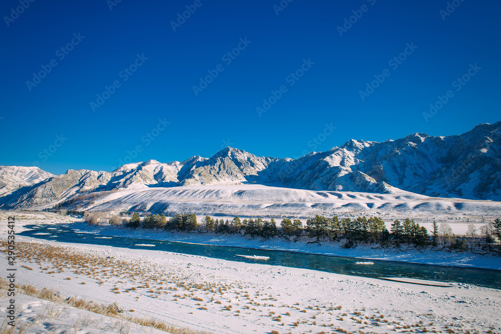 River flows through a snow-covered valley. Winter landscape of mountain peaks and blue sky. Fantastic panorama of wildlife, space for text.