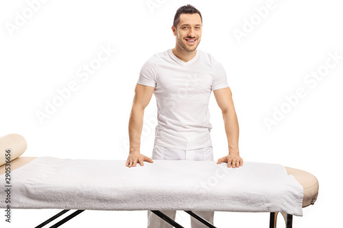Professional young masseur posing behind a massage bed photo