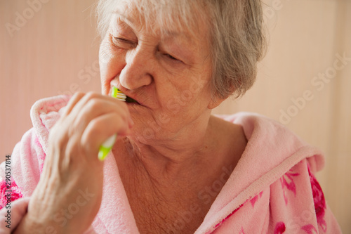 Elderly grandmother in pink terry bathrobe brushes her teeth in bathroom. Hygienic procedures. Pensioners in sanatorium