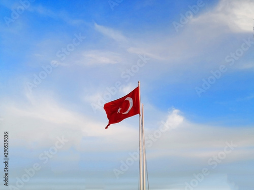 The national flag of Turkey, which has red background with the white star and crescent moon symbol, is waving over the blue sky. Selective focus and copyspace.