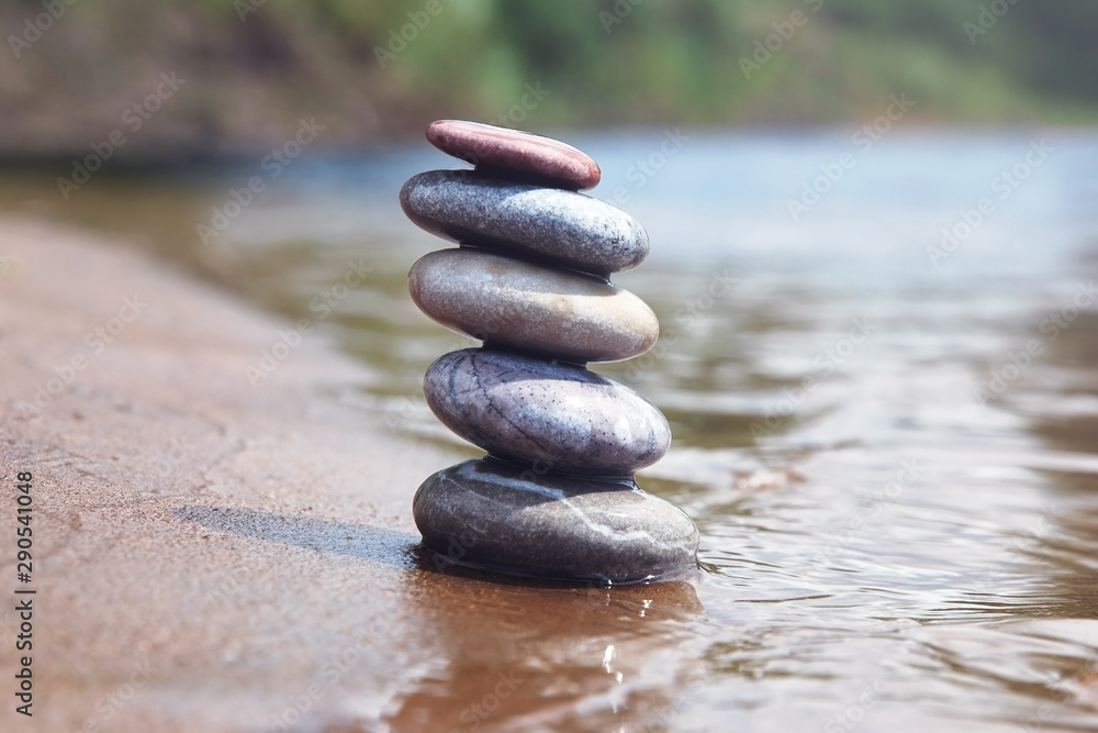 Stack of balancing pebble stones on sand and water edge. Zen symbol against blurred nature background. Stack of balancing pebble stones on sand and water edge. Zen symbol against blurred nature background.
