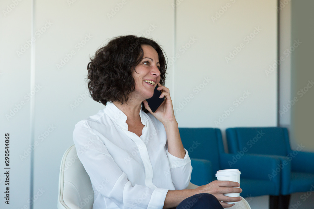 Happy businesswomen talking on cell while drinking coffee. Business woman sitting in office corridor, speaking on cellphone and laughing. Phone talk concept Happy businesswomen talking on cell while drinking coffee. Business woman sitting in office corridor, speaking on cellphone and laughing. Phone talk concept