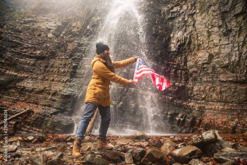 young caucasian adult female with usa flag in front of waterfall