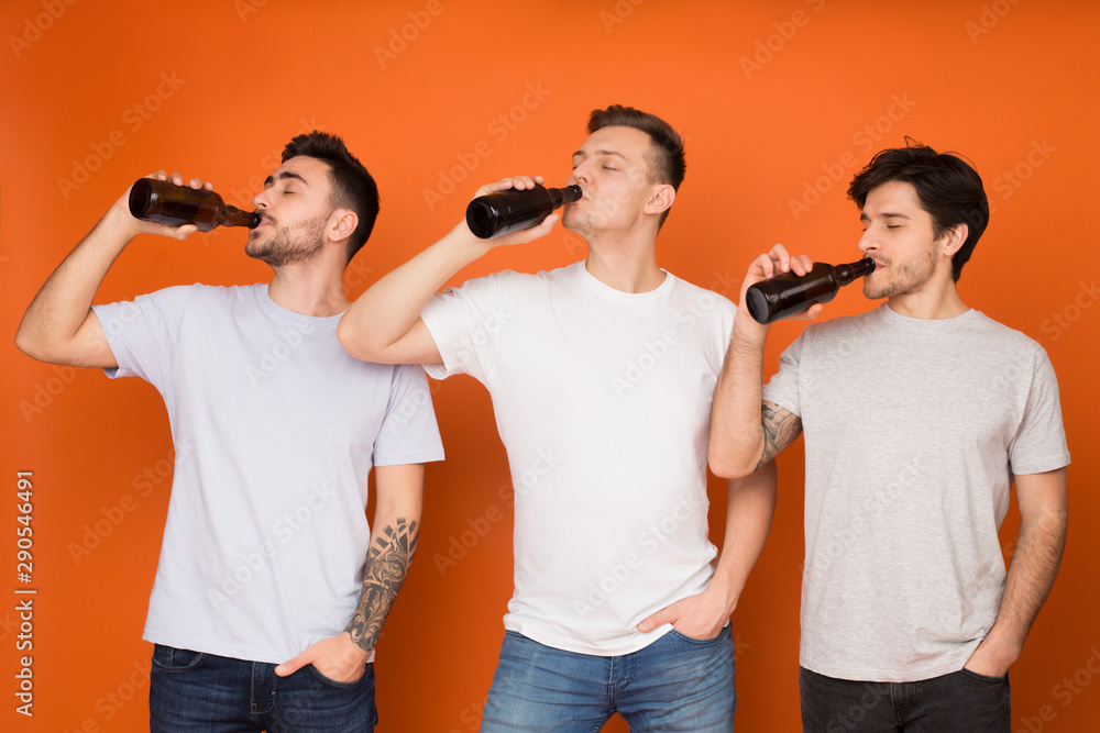 Three mates drinking beer from bottles, standing in row Three mates drinking beer from bottles, standing in row