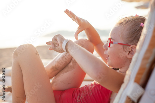 funny girl in glasses and a red bathing suit lies on a deck chair and plays
