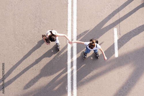 Girls friends rollerblading in city park holding each other hands 