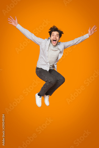 Crazy man jumping with raised arms over orange background