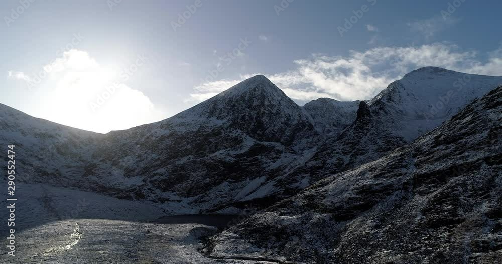 Wide, aerial, sun shines over snowy mountains in Ireland