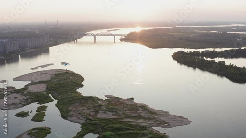 Parasail wing flying on golden sunset horizon landscape. Paraplane flying over river on city architecture background. Paraglider parachute sport aerial view photo