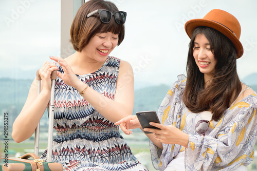 Two asian women using app on mobile phone, looking at screen of smart phone, texting, watching photos while traveling.
