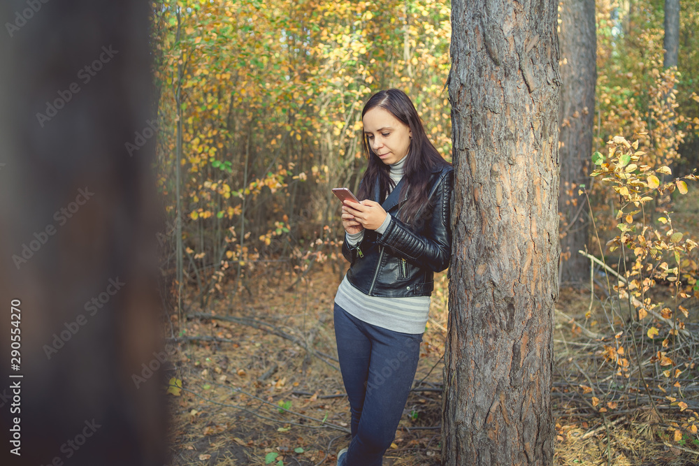 Woman uses a smarphone in the autumn forest. Female dials a message on the phone